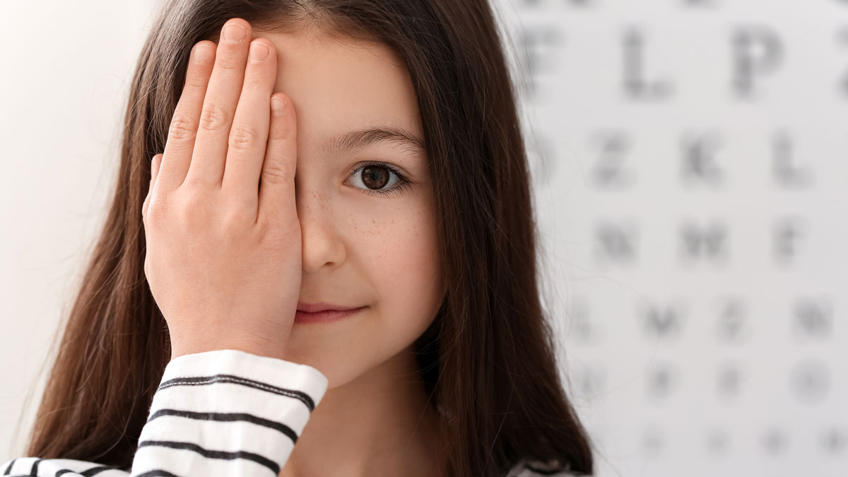 Young girl looking at the camera with a smile while covering one eye with her hand