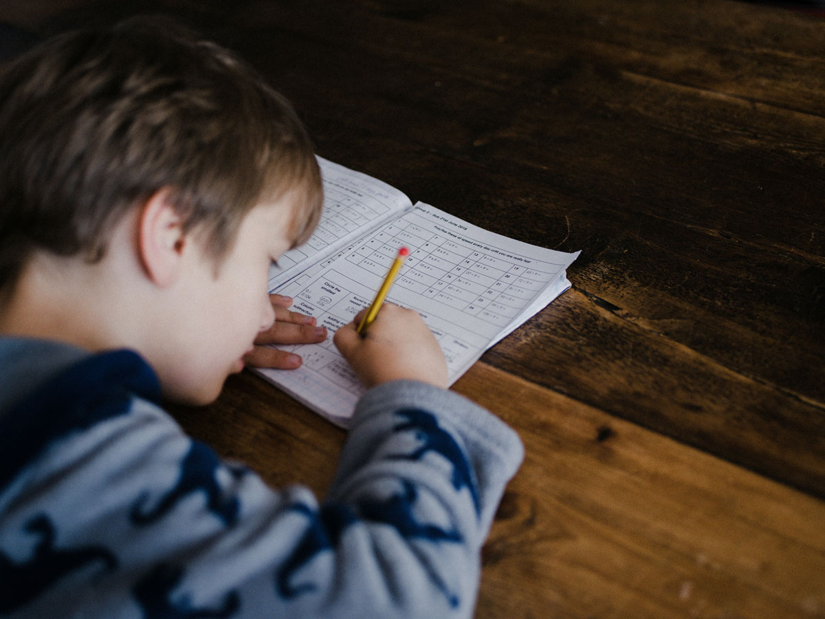 Young boy at a wooden desk writing in a notepad