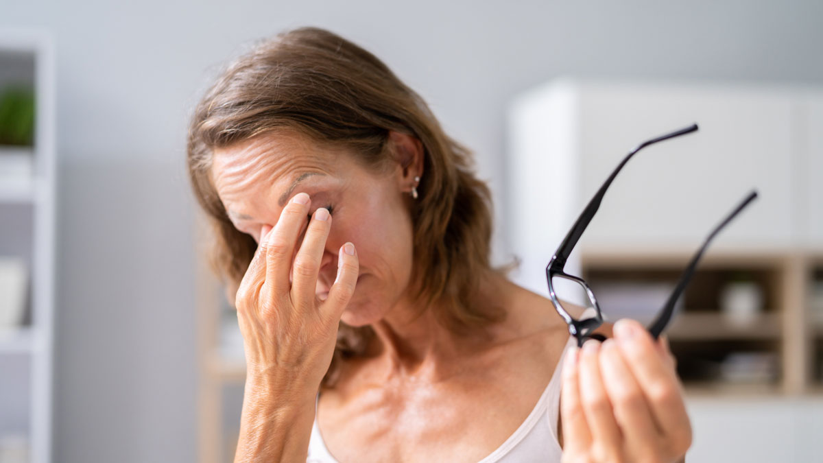 Woman holding her glasses in one hand and rubbing her eyes in discomfort with the other hand