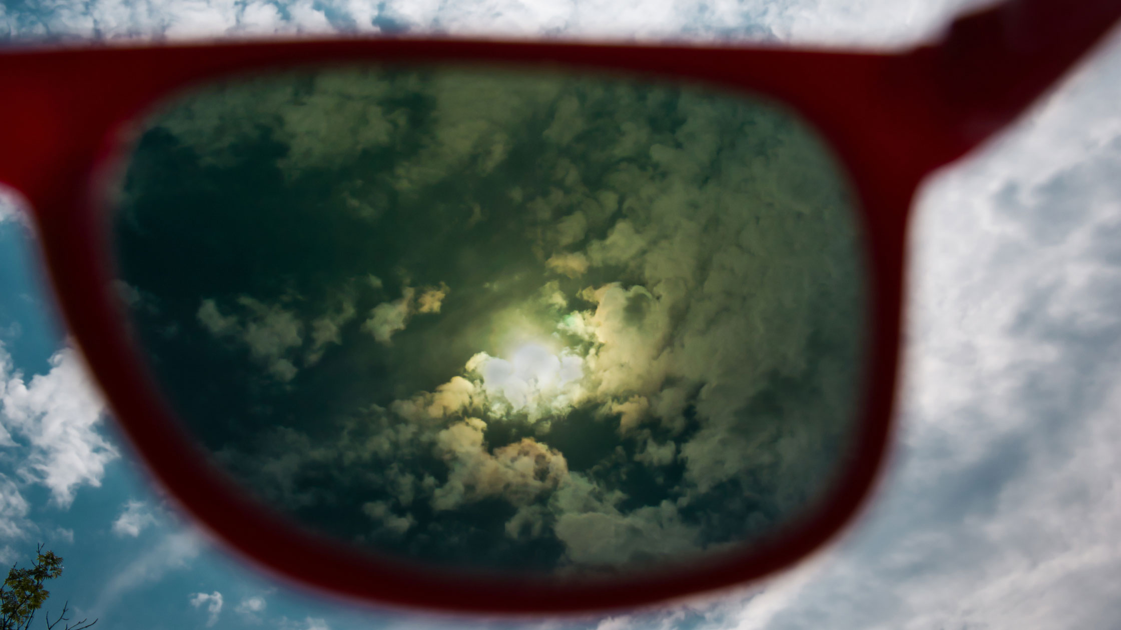 Poloarized reflection of sun behind clouds in the lens of sunglasses